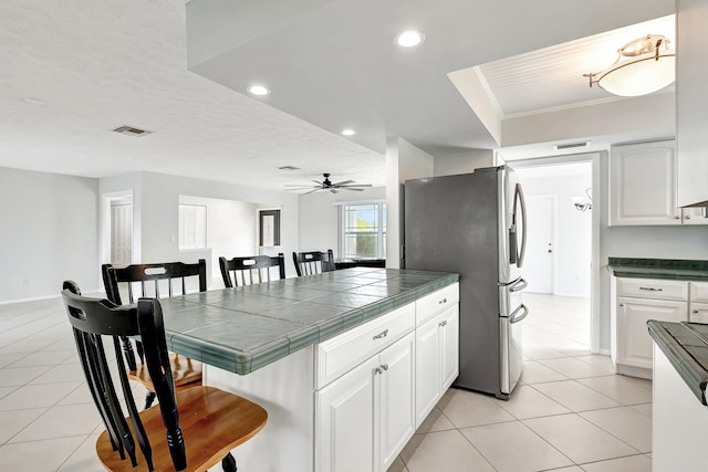 kitchen featuring white cabinets, tile countertops, stainless steel refrigerator, and a kitchen bar