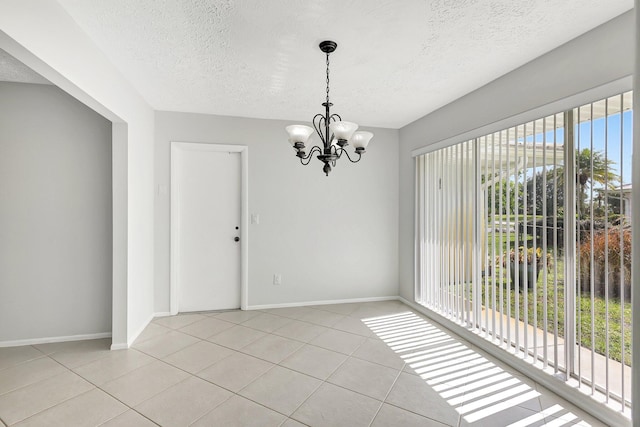 unfurnished dining area with light tile patterned floors, a textured ceiling, baseboards, and an inviting chandelier