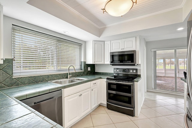 kitchen featuring white cabinets, a tray ceiling, stainless steel appliances, crown molding, and a sink