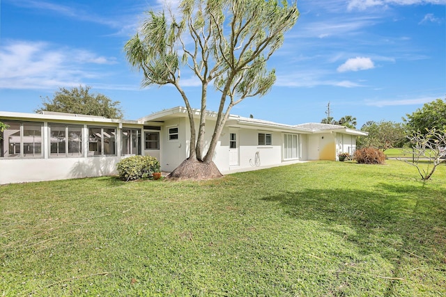 rear view of house with a sunroom, stucco siding, and a yard