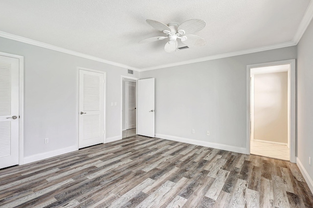 unfurnished bedroom with baseboards, a textured ceiling, ornamental molding, and wood finished floors