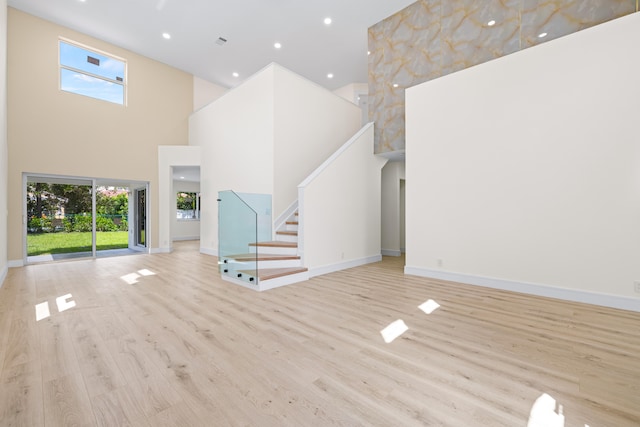 unfurnished living room featuring a towering ceiling and light hardwood / wood-style floors