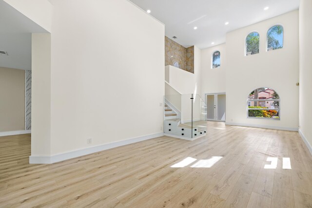 unfurnished living room featuring light hardwood / wood-style flooring and a towering ceiling