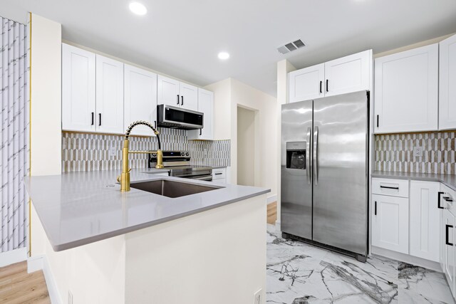 kitchen featuring white cabinets, stainless steel appliances, backsplash, and kitchen peninsula