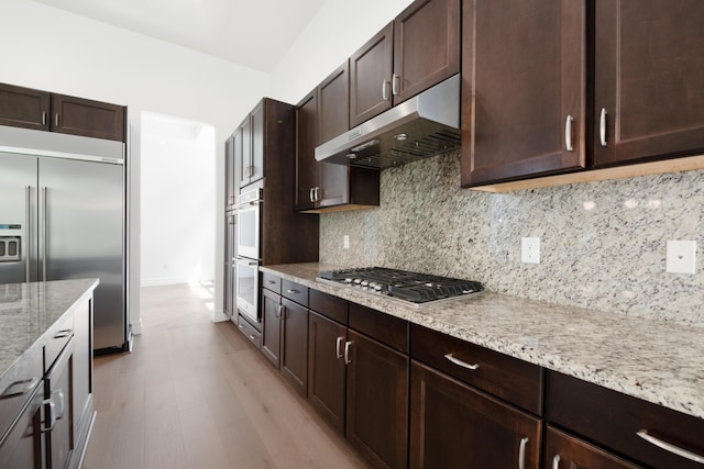 kitchen featuring light wood finished floors, appliances with stainless steel finishes, under cabinet range hood, and dark brown cabinetry
