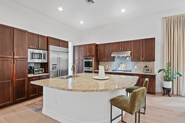 kitchen featuring built in appliances, decorative backsplash, sink, and a center island with sink