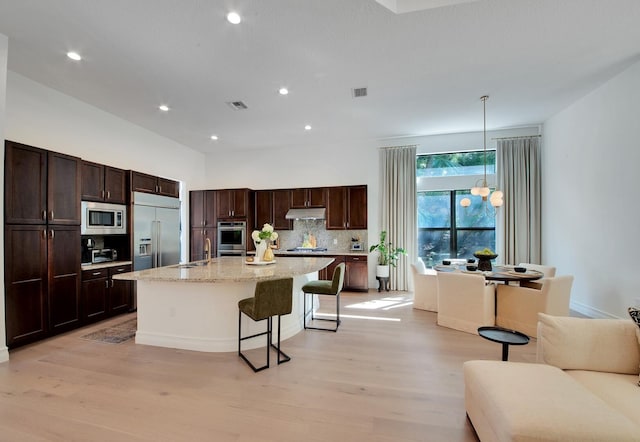 kitchen featuring a center island with sink, decorative light fixtures, built in appliances, sink, and a breakfast bar area