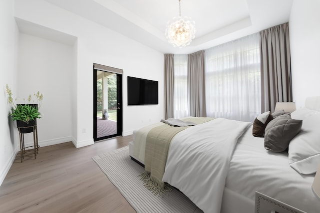 bedroom featuring access to exterior, an inviting chandelier, a tray ceiling, baseboards, and light wood-style floors