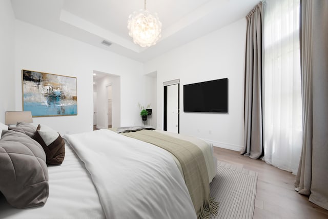 bedroom with wood finished floors, visible vents, an inviting chandelier, a tray ceiling, and baseboards