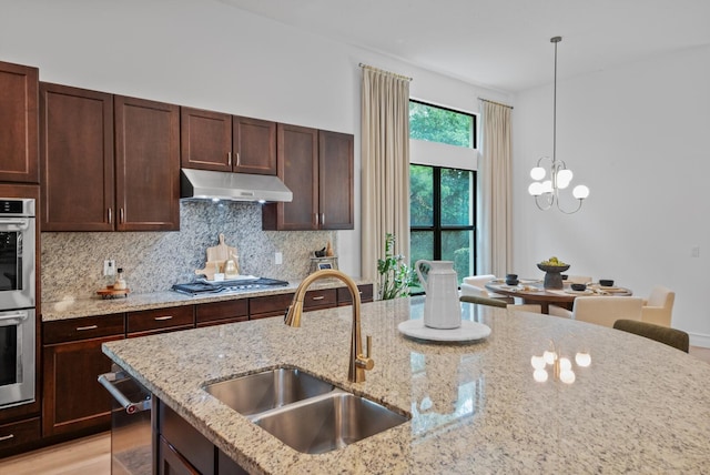 kitchen with sink, appliances with stainless steel finishes, light stone counters, and pendant lighting