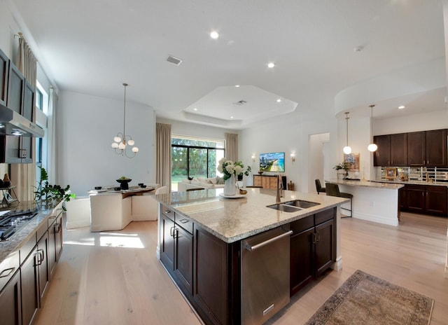 kitchen with appliances with stainless steel finishes, sink, a tray ceiling, decorative light fixtures, and an island with sink