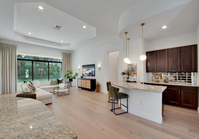 kitchen featuring a breakfast bar, light hardwood / wood-style flooring, decorative light fixtures, light stone counters, and a raised ceiling