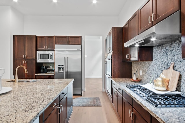 kitchen featuring built in appliances, light hardwood / wood-style floors, sink, light stone counters, and decorative backsplash