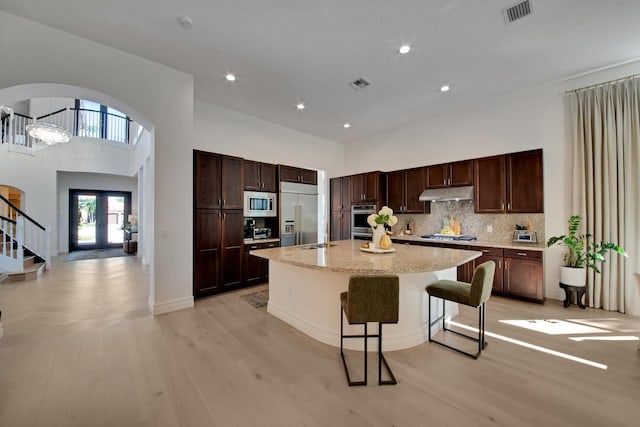 kitchen featuring built in appliances, a center island, a kitchen breakfast bar, a high ceiling, and backsplash