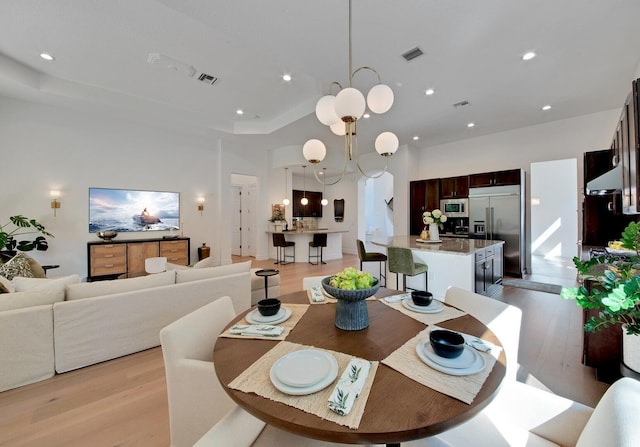 dining space with a raised ceiling, light hardwood / wood-style floors, and an inviting chandelier