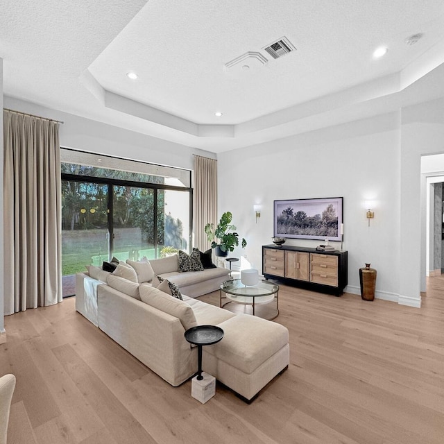 living room featuring light hardwood / wood-style flooring, a textured ceiling, and a tray ceiling