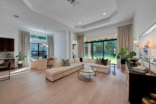 living room with light wood-type flooring, a wealth of natural light, a tray ceiling, and a chandelier