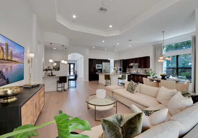 living room featuring a notable chandelier, a tray ceiling, and light hardwood / wood-style flooring