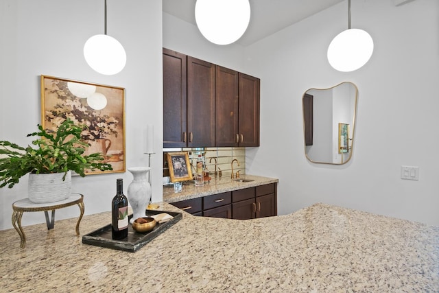 kitchen featuring lofted ceiling, decorative light fixtures, light stone countertops, sink, and dark brown cabinets