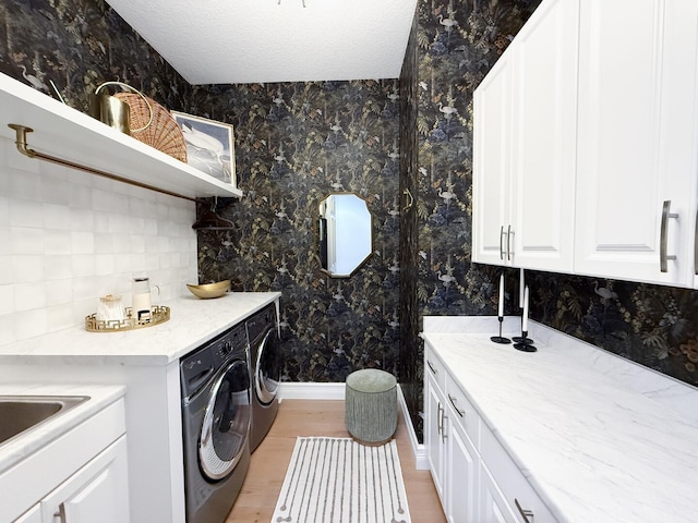 washroom featuring cabinet space, separate washer and dryer, light wood-style flooring, baseboards, and wallpapered walls