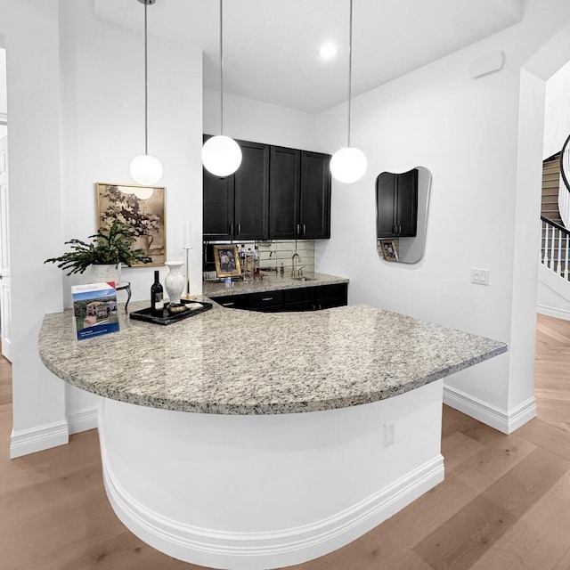 kitchen with pendant lighting, light hardwood / wood-style flooring, backsplash, light stone countertops, and kitchen peninsula