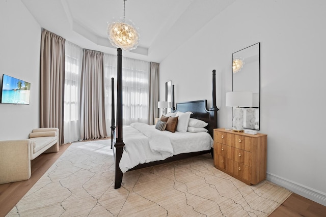 bedroom with light hardwood / wood-style flooring, a notable chandelier, and a raised ceiling