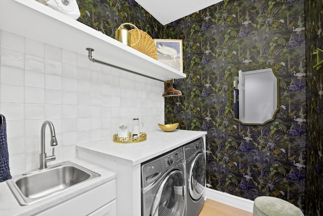 clothes washing area featuring baseboards, independent washer and dryer, wallpapered walls, and a sink