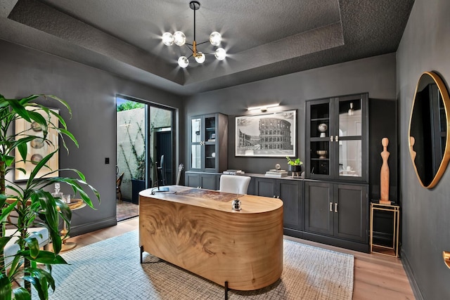 home office featuring a notable chandelier, light hardwood / wood-style floors, a tray ceiling, and a textured ceiling