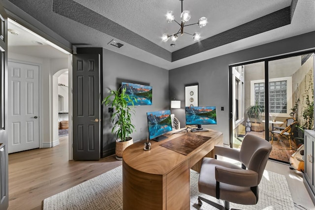 office area featuring a textured ceiling, a raised ceiling, an inviting chandelier, and light hardwood / wood-style flooring