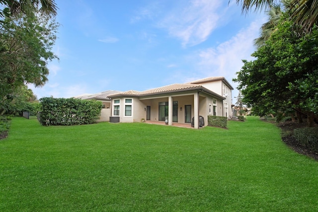back of house with a patio, a tile roof, stucco siding, and a lawn