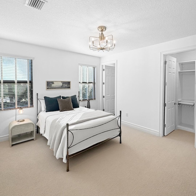 bedroom featuring an inviting chandelier, a spacious closet, carpet floors, and a textured ceiling