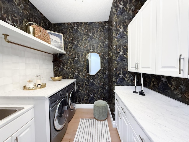 clothes washing area featuring washer and dryer, cabinets, light wood-type flooring, and a textured ceiling