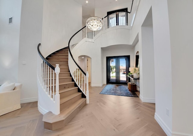 foyer entrance with a high ceiling, light parquet flooring, and an inviting chandelier