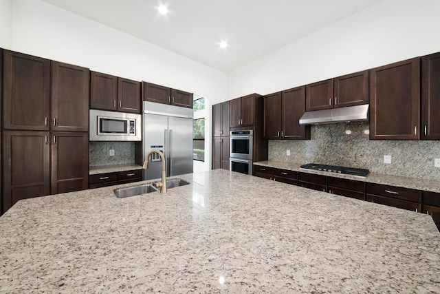 kitchen featuring a sink, dark brown cabinetry, built in appliances, under cabinet range hood, and decorative backsplash