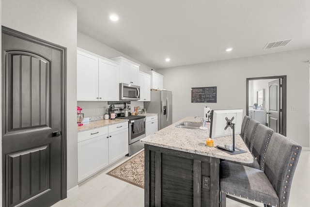 kitchen with stainless steel appliances, light stone counters, a center island with sink, and sink