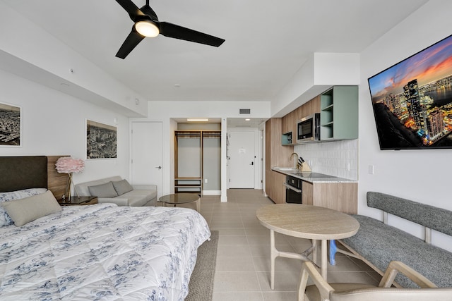 bedroom with light tile patterned flooring, sink, ceiling fan, and a closet