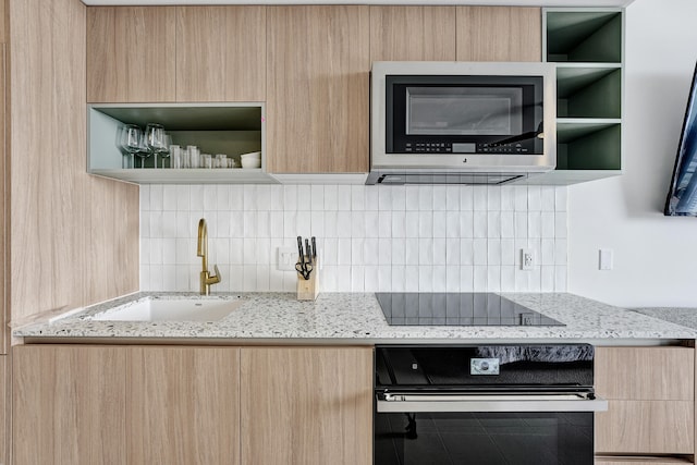 kitchen with light stone counters, light brown cabinets, sink, backsplash, and black appliances