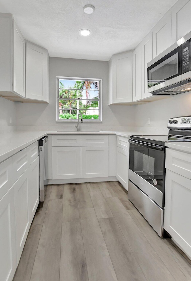 kitchen featuring light hardwood / wood-style flooring, appliances with stainless steel finishes, sink, and white cabinetry