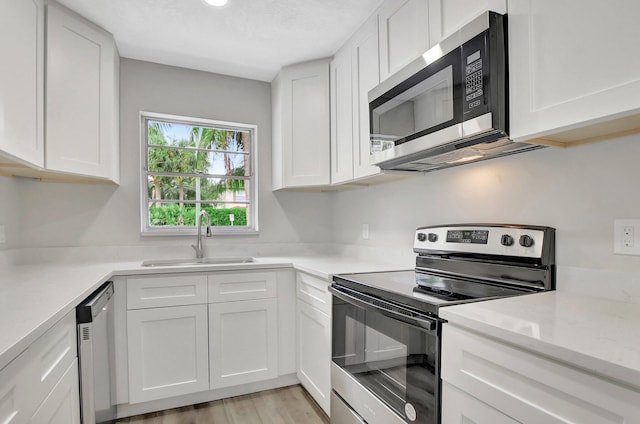 kitchen featuring light stone counters, sink, white cabinetry, stainless steel appliances, and light wood-type flooring