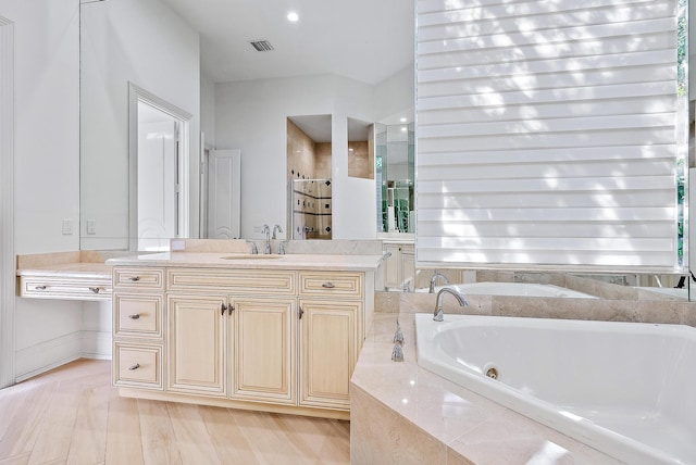 bathroom with hardwood / wood-style flooring, a relaxing tiled tub, and vanity