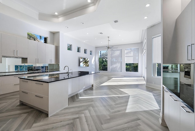 kitchen with a raised ceiling, decorative light fixtures, sink, an island with sink, and light parquet flooring