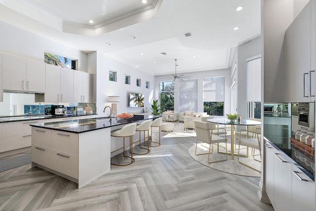 kitchen featuring an island with sink, light parquet floors, white cabinetry, and tasteful backsplash