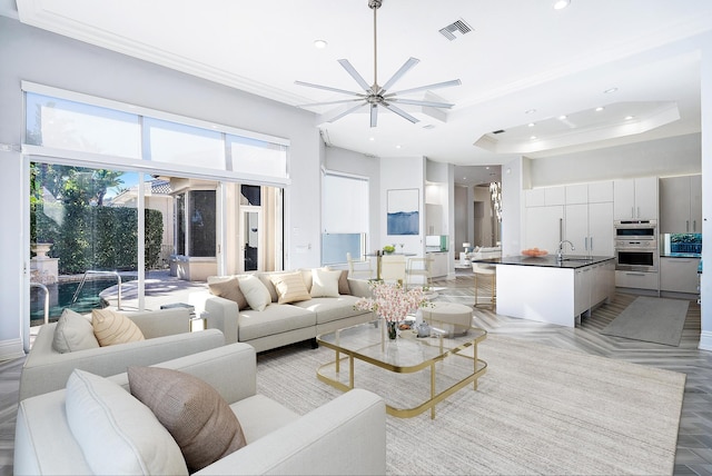 living room with ornamental molding, ceiling fan, a tray ceiling, and sink