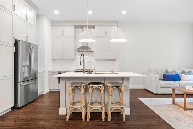 kitchen with dark hardwood / wood-style flooring, stainless steel refrigerator with ice dispenser, decorative light fixtures, a breakfast bar area, and a center island with sink