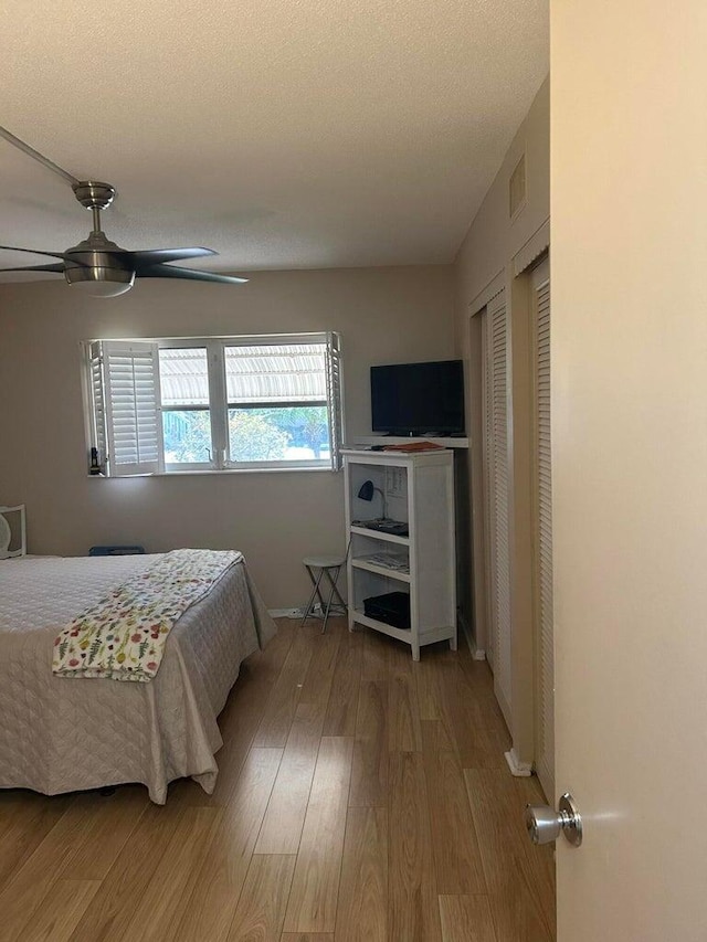 bedroom featuring multiple closets, ceiling fan, wood-type flooring, and a textured ceiling