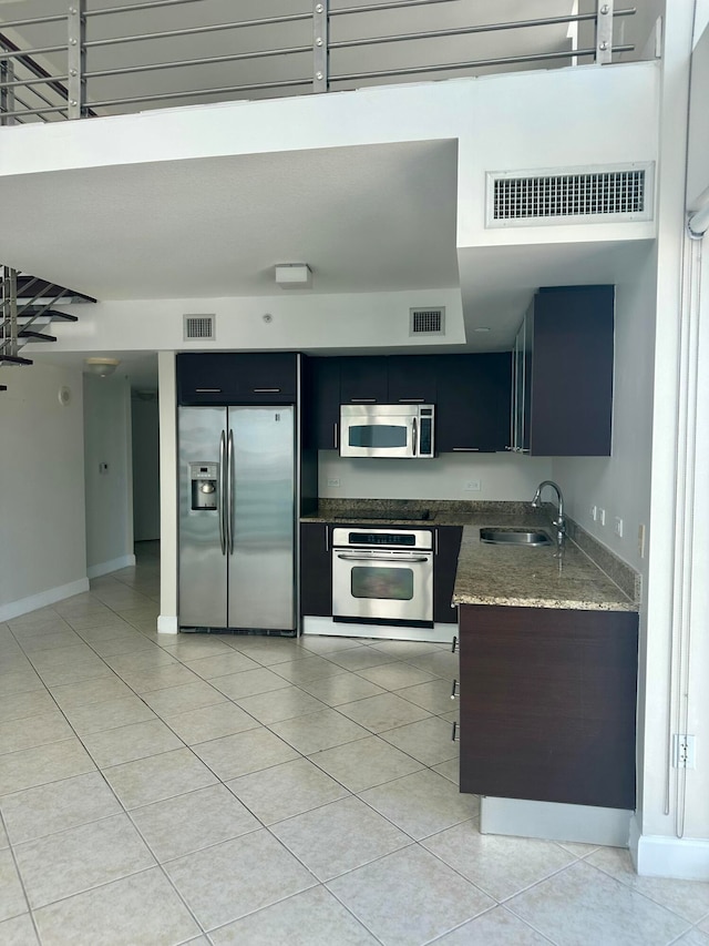 kitchen with appliances with stainless steel finishes, light tile patterned floors, dark stone countertops, and sink