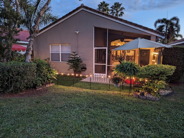 property exterior at dusk with a yard and ceiling fan