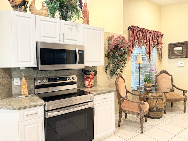 kitchen with appliances with stainless steel finishes, light tile patterned floors, tasteful backsplash, and white cabinetry