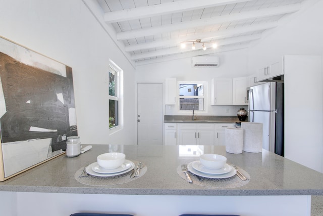 kitchen featuring white cabinets, kitchen peninsula, lofted ceiling with beams, and stainless steel refrigerator