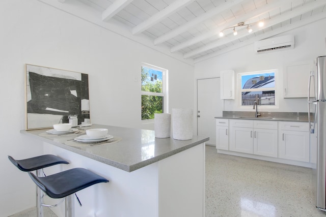 kitchen with sink, a wall mounted air conditioner, vaulted ceiling with beams, white cabinetry, and a breakfast bar